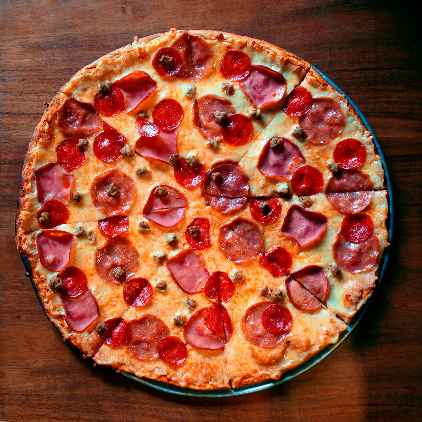 En oppskåret pizza med pepperoni og skinke på et mørkt trebord